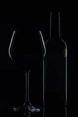 Wine bottle and a glass of red wine in the background light. Dark mood