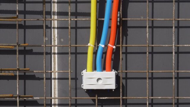 CLOSE UP: Electricity and internet installation tubing runs along house under construction. Three corrugated plastic conduits converge into single socket set installed on outer side of unfinished wall
