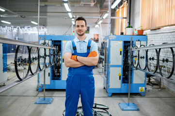 Worker in uniform poses on bicycle wheel factory