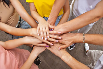 Friends cross their arms on the background of paving slabs. Many hands of youth. top shooting angle.