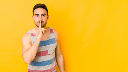 Young caucasian man isolated on yellow bakground keeping a secret or asking for silence.