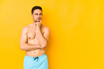 Young caucasian man with swimsuit isolated on yellow background Young caucasian man with trthinking and looking up, being reflective, contemplating, having a fantasy.