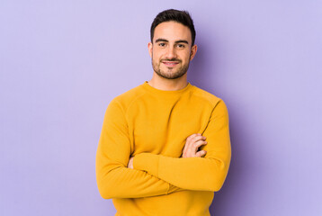 Young caucasian man isolated on purple background who feels confident, crossing arms with determination.