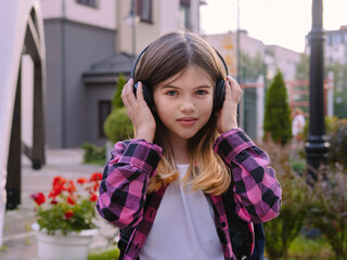 little girl in a plaid shirt listening to music on headphones