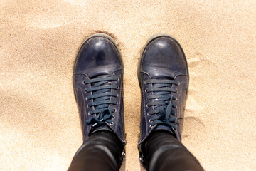 Female feet in boots on the sand, top view