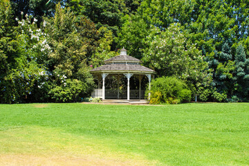 a beautiful summer landscape with a wooden gazebo surrounded by lush green trees, plants and grass...