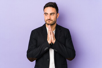 Young caucasian man isolated on purple background praying, showing devotion, religious person looking for divine inspiration.
