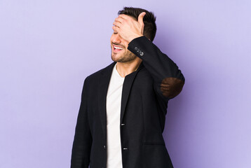 Young caucasian man isolated on purple background laughs joyfully keeping hands on head. Happiness concept.