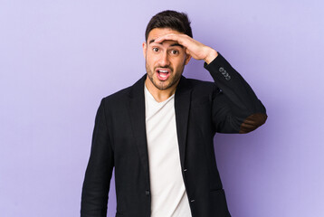 Young caucasian man isolated on purple background looking far away keeping hand on forehead.