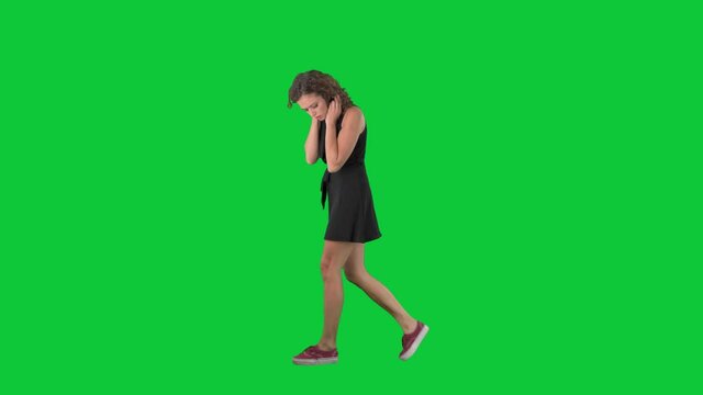Concerned young woman walking and looking down searching something lost. Full body side view on green screen chroma key background. 
