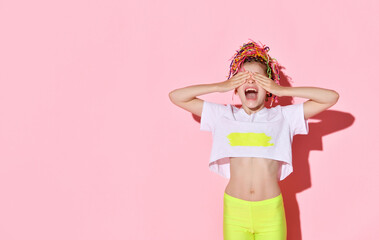 Teenage female with african pigtails has covered her eyes by palms and screaming while posing on pink studio background