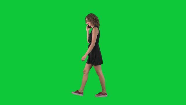 Happy relaxed young woman walking and talking on the phone with friend. Full body side view on green screen chroma key background. 