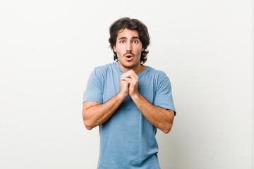 Young handsome man against a white background praying for luck, amazed and opening mouth looking to front.