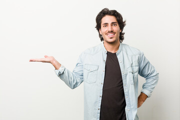 Young handsome man against a white background showing a copy space on a palm and holding another hand on waist.