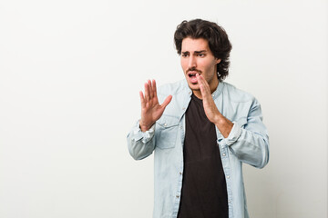 Young handsome man against a white background shouts loud, keeps eyes opened and hands tense.