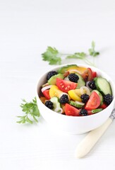 Vegetable berry salad of fresh yellow, red, black tomatoes, cucumbers, onions and blackberries in a bowl on a white background