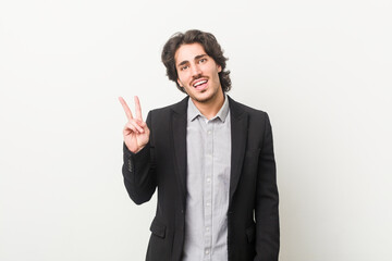Young business man against a white background joyful and carefree showing a peace symbol with fingers.