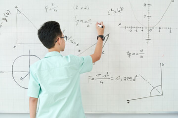 Schoolboy in glass writing geometry equation on whiteboard, view from the back
