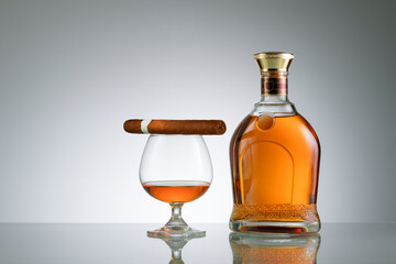 close up view of cigar, bottle of cognac and a glass aside on grey back. 