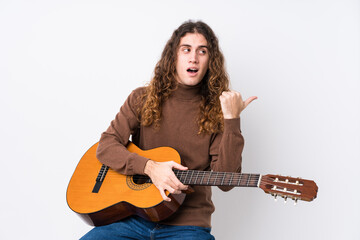 Young caucasian man playing guitar isolated points with thumb finger away, laughing and carefree.