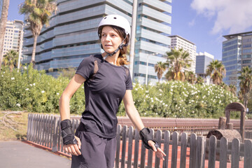 Young roller skater caucasian woman in the white helmet and black sporty clothes, sunny day, skatepark, urban environment.