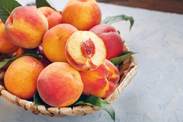 Naklejka na ściany i meble Ripe peaches in a wicker basket on a stone gray table with a juicy peach slice with a stone pit.