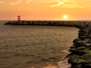 Sunset on the red semaphore entrance of the harbor channel built with concrete cubic blocks
