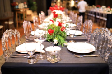 A blurred image of a dinner table with red roses. And green decorative leaves
