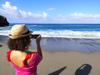 Woman from behind with hat photographing the sea