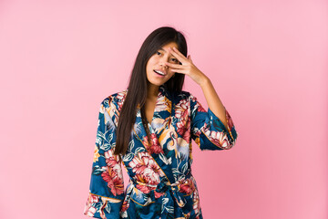 Young asian woman wearing a kimono pajamas blink at the camera through fingers, embarrassed covering face.