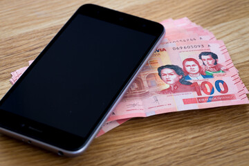  Bolivian currency, One hundred Bolivianos banknotes lying together with a mobile phone on the...