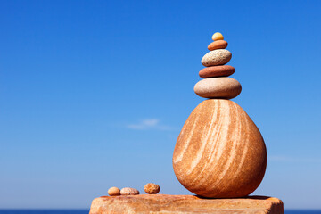 Rock zen pyramid of white and pink pebbles on a background of blue sky and sea.