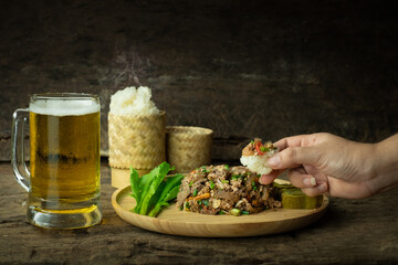 Using a hand to eat sticky rice and spicy minced pork salad with beer, Larb is traditional Thai food is the culture of the people in the northeast of Thailand