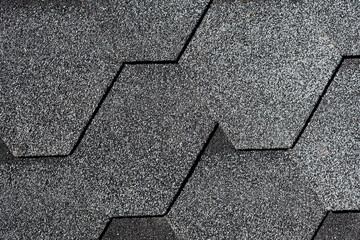 Closeup of gray asphalt roof shingles texture. Roof covered by hexagonal soft shingles or tiles....