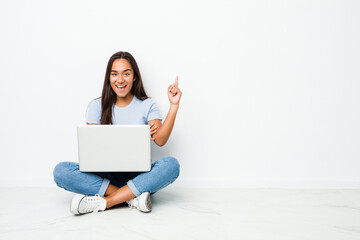Young mixed race indian woman sitting working on laptop smiling cheerfully pointing with forefinger away.