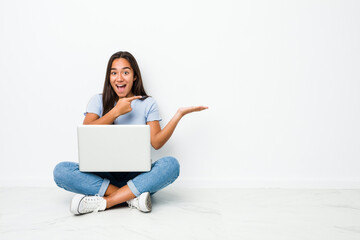 Young mixed race indian woman sitting working on laptop excited holding a copy space on palm.