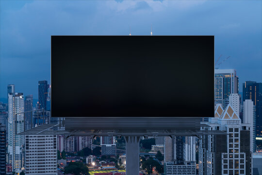 Blank black road billboard with Kuala Lumpur cityscape background at night time. Street advertising poster, mock up, 3D rendering. Front view. Concept of marketing to promote or sell idea or product.