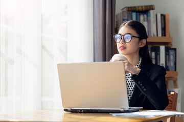 Young Asian business woman drinking coffee and using her laptop in her office