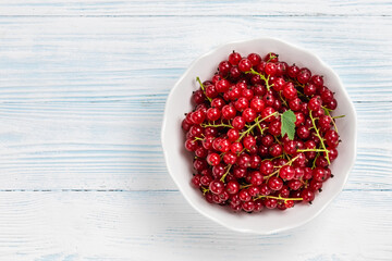 Red currant in a bowl on white wooden background. Top view, space for text.
