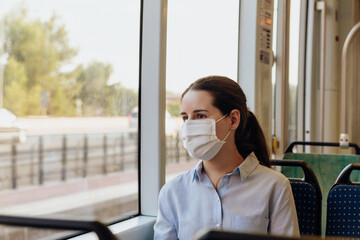 Stock photo of a young woman wearing a face mask traveling by public transport. She is looking out the window