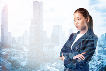 Prosperous Asian businesswoman in suit in crossed arms pose. Bangkok cityscape. The concept of woman in business. Financial downtown. Double exposure.