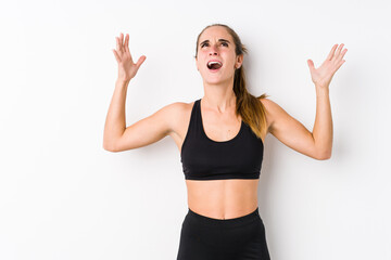 Young caucasian fitness woman posing in a white background screaming to the sky, looking up, frustrated.