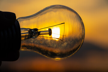 incandescent light bulb in hand on sunset background close- up