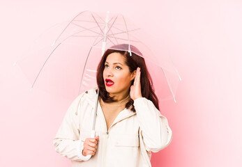 Middle age latin woman wearing an umbrella isolated trying to listening a gossip.