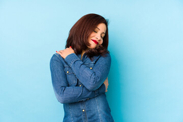 Middle age latin woman isolated on a blue background hugs, smiling carefree and happy.