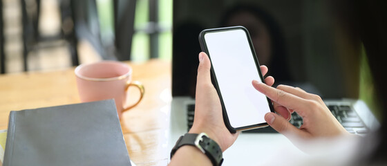 Cropped image of a woman's hand is using a mockup smartphone over a computer laptop as a background.