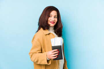 Middle age latin woman holding a passport isolated looks aside smiling, cheerful and pleasant.