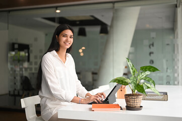 A beautiful woman is using a computer tablet with a keyboard case and stylus pen at the modern work...
