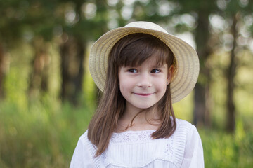 Happy little girl on the forest. Cute smiling girl in a white dress looks away