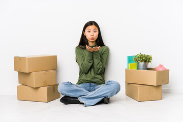 Young chinese woman moving to a new home folding lips and holding palms to send air kiss.